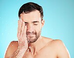 Water drop, skincare and man with hand on face, morning cleaning treatment isolated on blue background. Facial hygiene, splash and male model grooming for health, wellness and spa skin care in studio