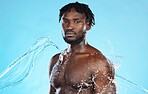 Skincare, shower and portrait of a black man with a water splash isolated on a blue background. Cleaning, beauty and African model for grooming, hygiene and care of body on a studio backdrop