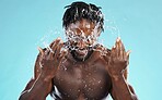 Water, splash and cleaning with a model black man in studio on a blue background for hydration or hygiene. Bathroom, skincare or wellness with a young male wahsing his face for natural skin treatment