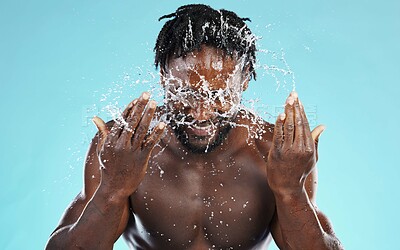 Buy stock photo Water, splash and cleaning with a model black man in studio on a blue background for hydration or hygiene. Bathroom, skincare or wellness with a young male wahsing his face for natural skin treatment