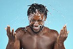 Water splash, cleaning and hygiene with a model black man in studio on a blue background for hydration. Bathroom, skincare and wellness with a young male wahsing his face for natural skin treatment