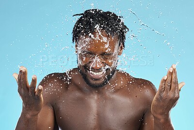 Buy stock photo Water splash, cleaning and hygiene with a model black man in studio on a blue background for hydration. Bathroom, skincare and wellness with a young male wahsing his face for natural skin treatment