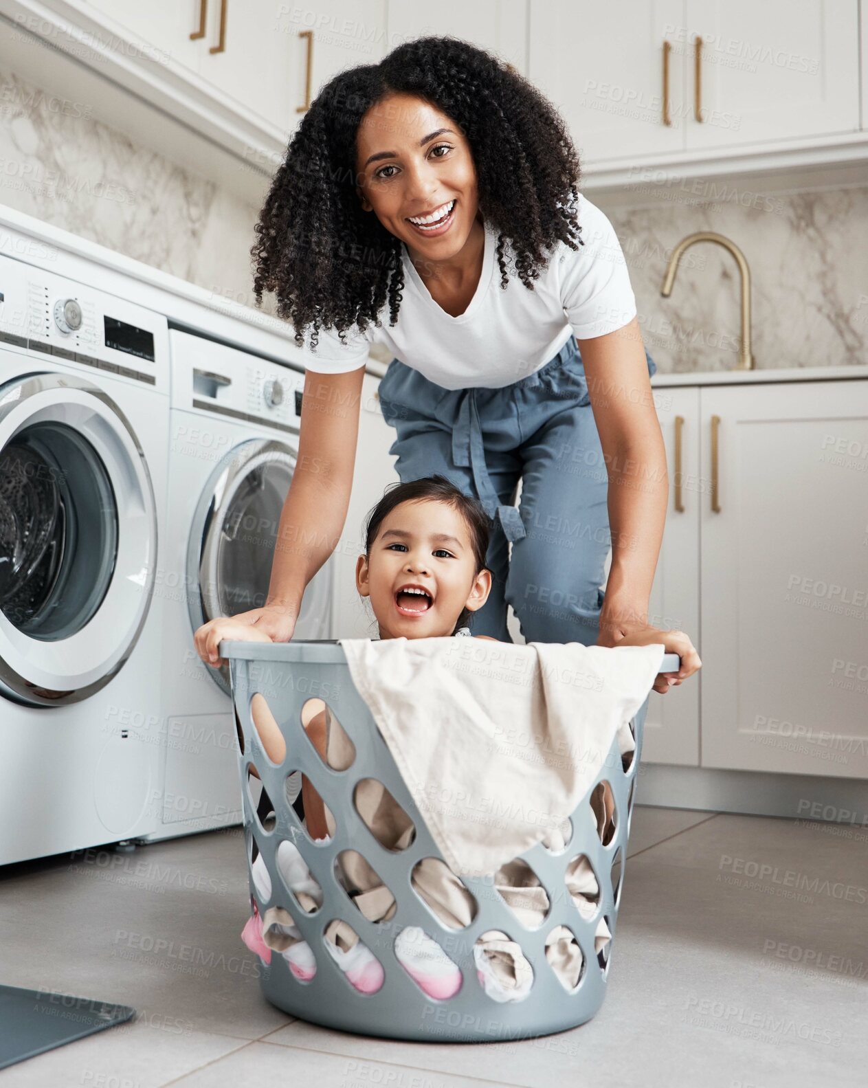 Buy stock photo Happy mother with her child in a washing basket at their home while doing laundry together. Happiness. housework and portrait of a young woman having fun with her girl kid while cleaning the house.