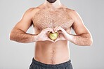 Man, fitness and heart hands with apple in studio isolated on a gray background. Food, wellness and male model with love hand gesture, fruits for nutrition or healthy diet, vitamin c or minerals.