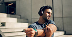 Fitness, headphones and man stretching arms on stairs in city, workout and exercise for body health. Music, serious athlete and person warm up on steps in urban town, listening to audio and thinking