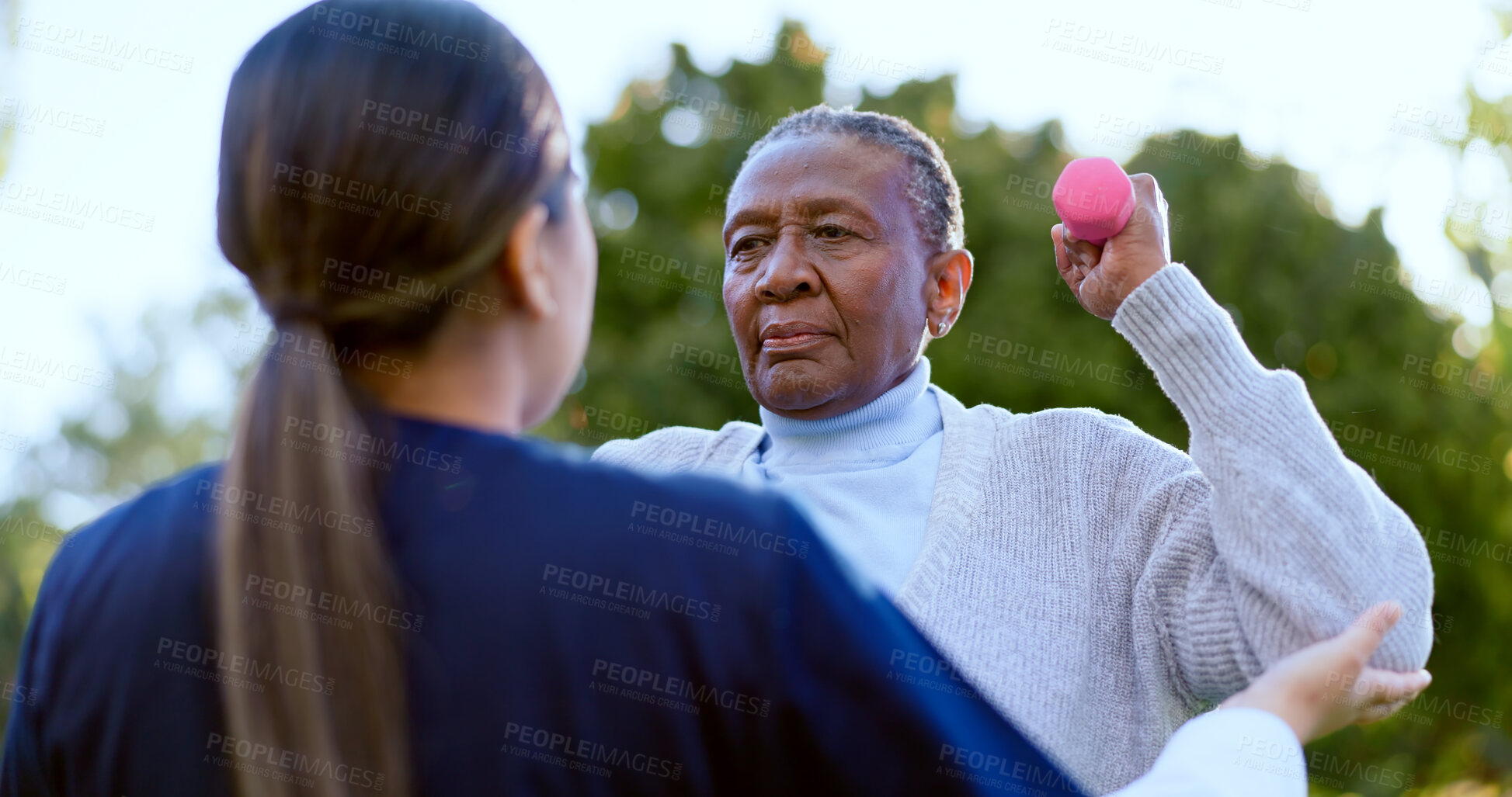 Buy stock photo Dumbbell, exercise and a senior black woman with a nurse outdoor in a garden together for physiotherapy. Fitness, health or wellness with an elderly patient and medical nurse in the yard to workout