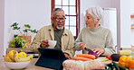 Senior couple, cooking and tablet in kitchen with knife, vegetables and tea cup for conversation. Interracial marriage, elderly woman and old man with touchscreen for video, food or nutrition in home