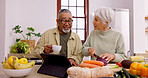 Senior couple, cooking and tablet in home kitchen with knife, vegetables and tea cup for conversation. Interracial marriage, elderly woman and old man with touchscreen for video, food and nutrition