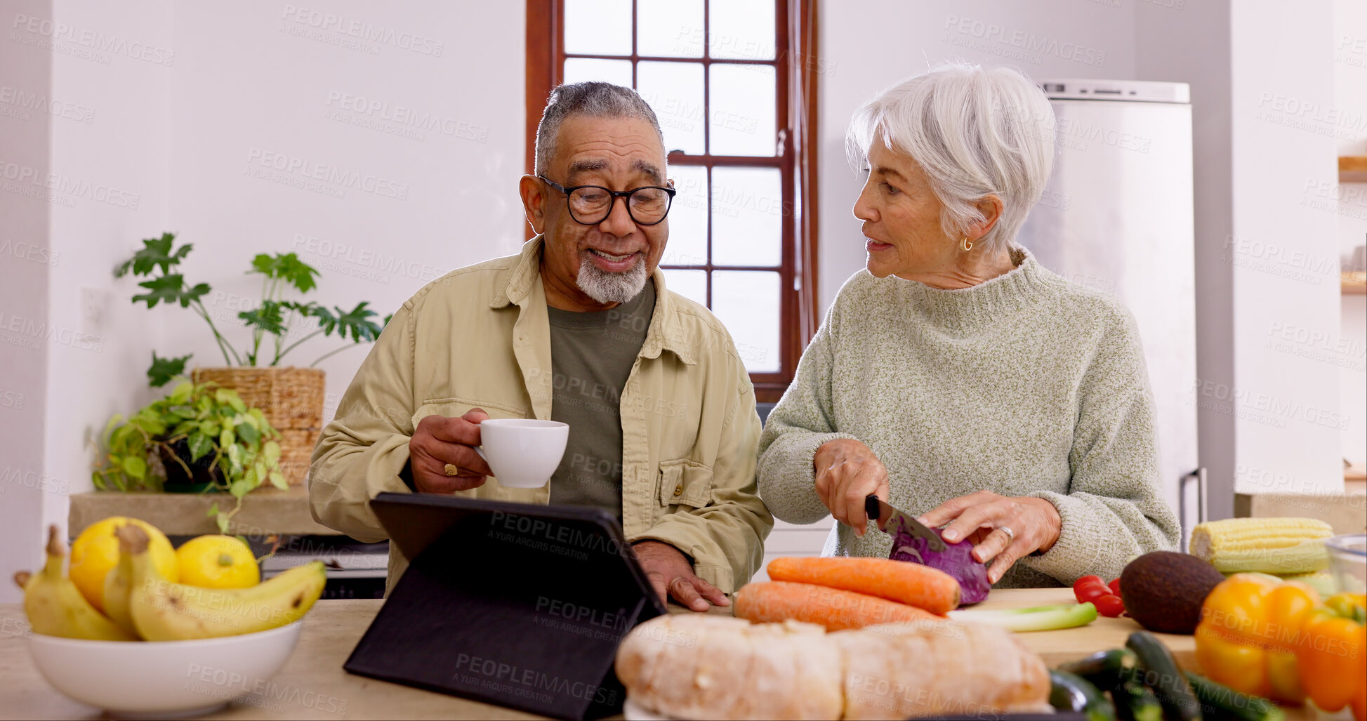 Buy stock photo Senior couple, cooking and tablet in home kitchen with knife, vegetables and tea cup for conversation. Interracial marriage, elderly woman and old man with touchscreen for video, food and nutrition