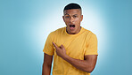 Pointing, shock and portrait of man in a studio with mockup for marketing, advertising or promotion. Surprise, wow and young male person with a show hand gesture isolated by blue background.
