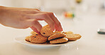Hands, cookies and plate on table in home kitchen, eating or hungry for sweets at breakfast. Closeup, biscuits and sugar food of person, dessert or confectionery snack for unhealthy diet in nutrition