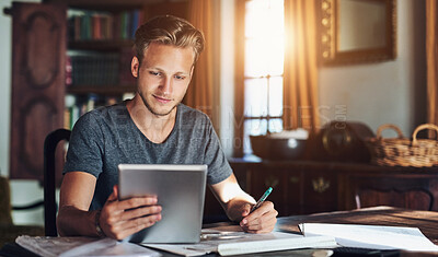 Buy stock photo Shot of a young man using a digital tablet while working on a project at home