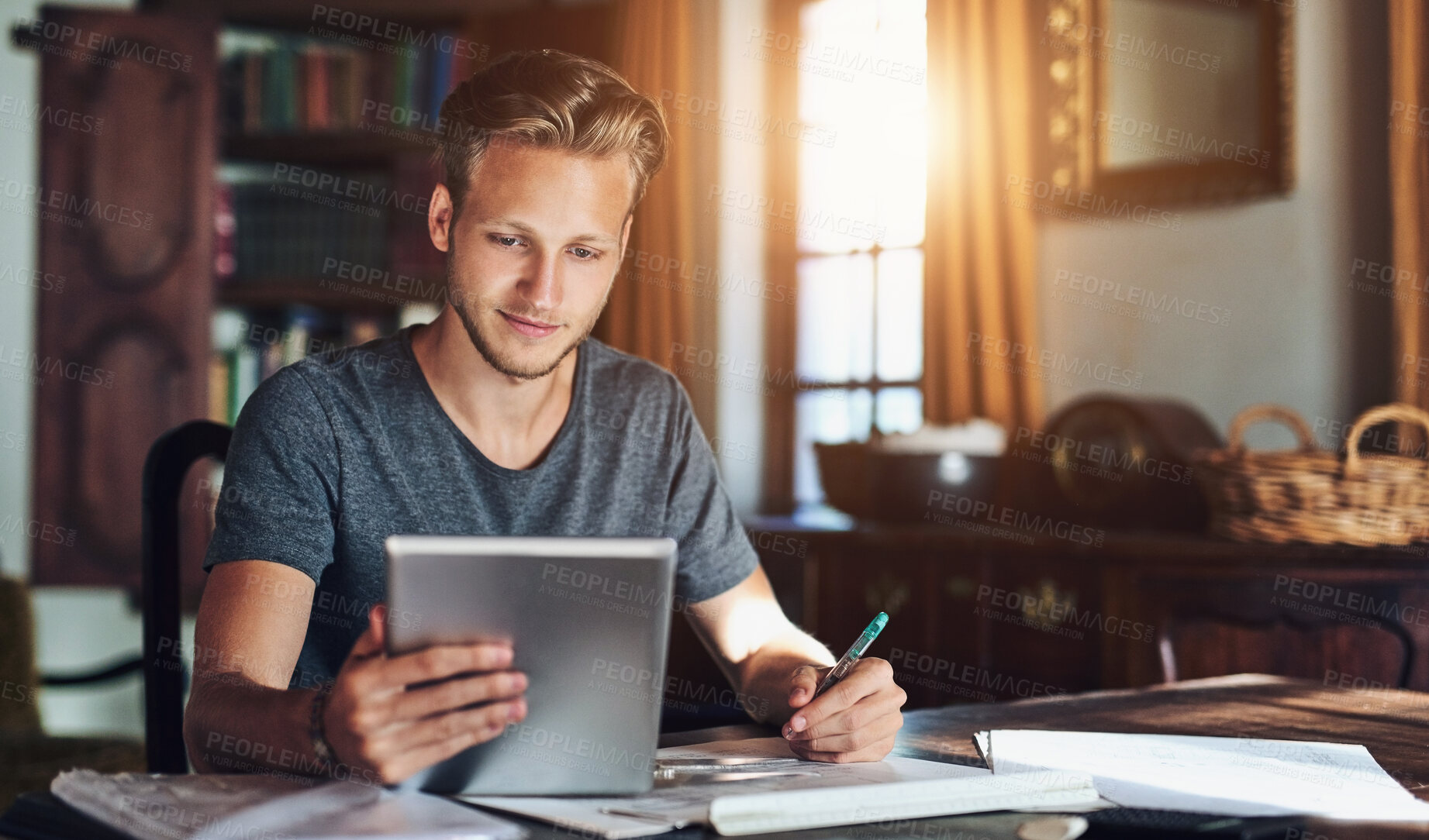 Buy stock photo Shot of a young man using a digital tablet while working on a project at home