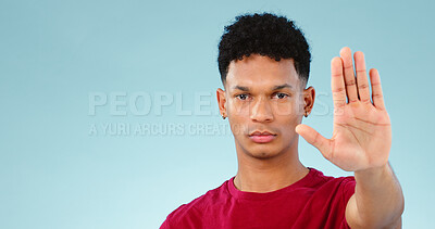 Man, hand and stop in studio portrait with forbidden warning, rejection and negative by blue background. Face, palm and sign language for defence sign or no, deny and wait for frustrated in mockup