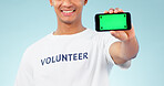 Hand, phone and green screen with a volunteer man in studio on blue background for marketing or charity. Smile, space or advertising and a person showing chromakey on a display with tracking markers