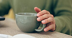 Closeup, hand and cup for coffee in home for relaxing, comfort or delicious taste in morning. Person, entrepreneur and remote work with hot beverage, tea or cappuccino for drinking on table in office