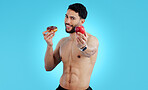 Happy man, portrait and apple with donut for diet, health or nutrition against a blue studio background. Male person or athlete showing natural organic red fruit with chocolate desert on mockup space