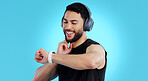 Happy man, headphones and checking watch for pulse in fitness against a blue studio background. Male person, athlete or model looking at wristwatch for monitoring performance or heart rate on mockup