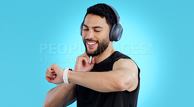 Buy stock photo Happy man, headphones and checking watch for pulse in fitness against a blue studio background. Male person, athlete or model looking at wristwatch for monitoring performance or heart rate on mockup