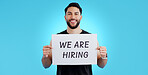 Portrait, smile and man with we are hiring, poster or announcement in studio on blue background. Recruitment, banner and face of male model with news, announcement or business, opportunity or offer