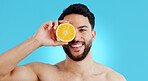 Orange, skincare or portrait of man in studio for vitamin C, natural cosmetics or healthy diet on blue background. Fruit, beauty and model face with citrus skin detox, cleaning or wellness nutrition