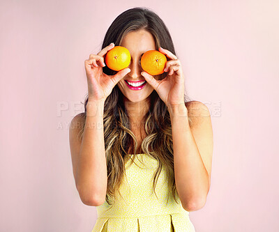 Buy stock photo Studio shot of a young woman holding up oranges in front of her eyes