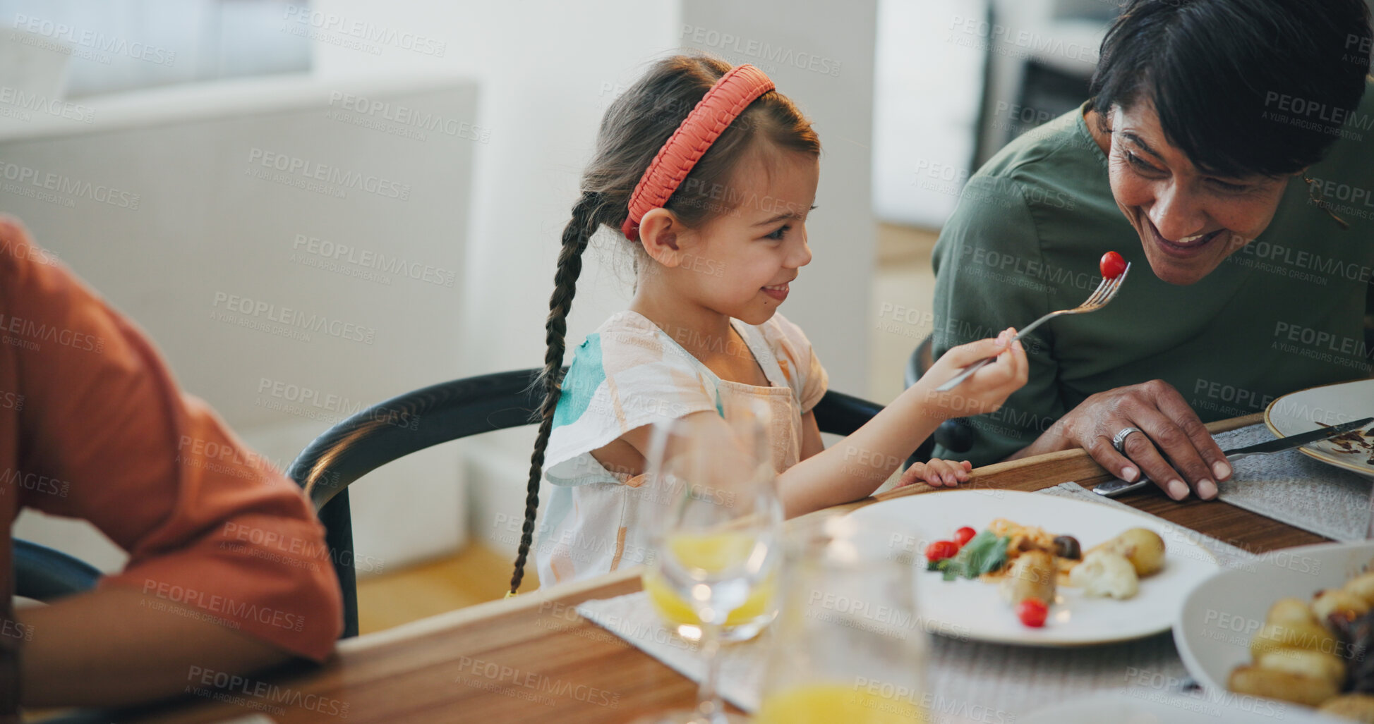 Buy stock photo Food, family and a girl feeding her grandmother at a dining room table while in their home for a visit together. Love, smile and a senior woman eating a meal with her happy grandchild in an apartment