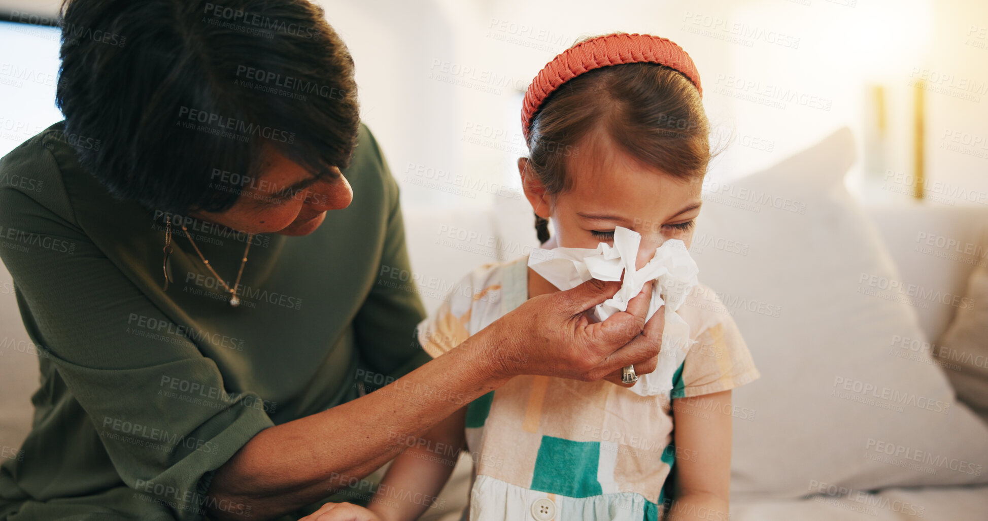 Buy stock photo Grandmother, sick kid and sneeze in home living room for allergy, covid or virus on sofa. Grandma, girl child and tissue for cold, flu and bacteria, disease and care or mature woman help blowing nose