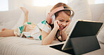 Happy little girl, tablet and headphones on sofa for elearning, entertainment or streaming at home. Female person, child or kid smile on technology in relax for movie, education or learning at house