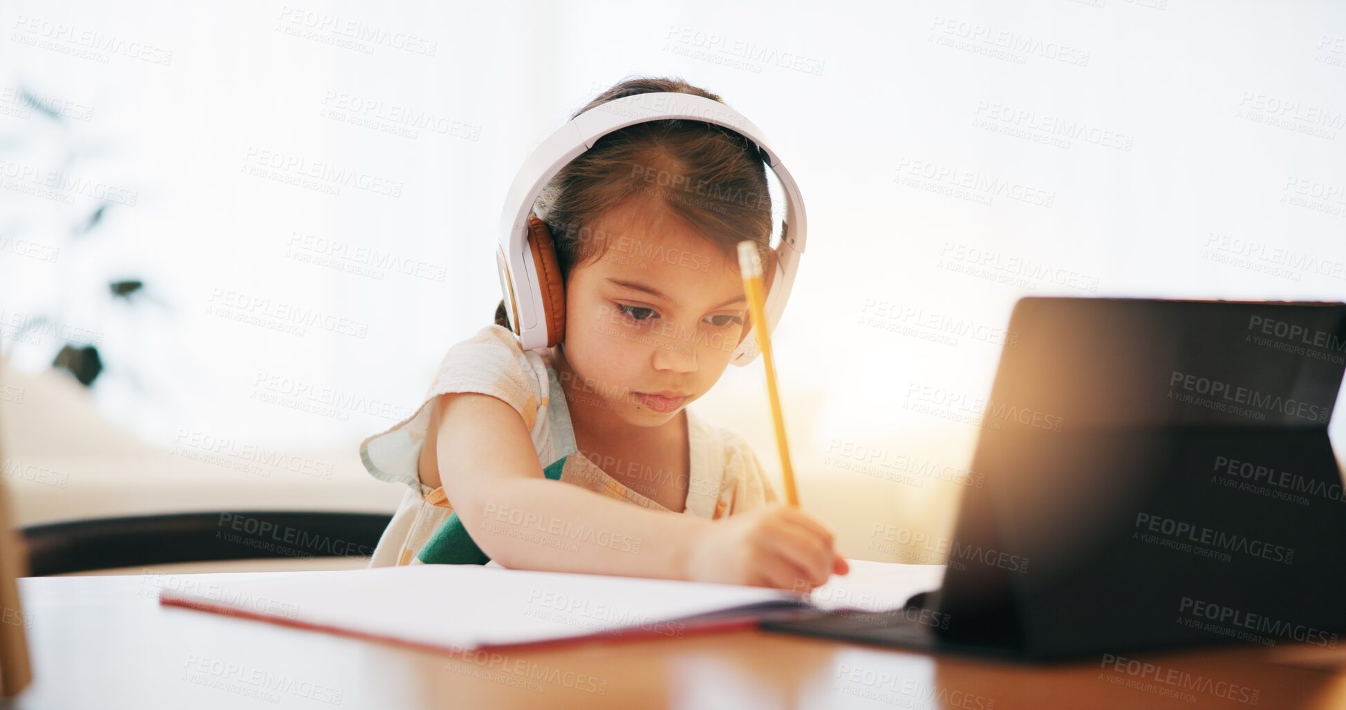 Buy stock photo Girl, headphones and writing in book for elearning, education or study on desk at home. Female person, child or kid taking notes with tablet, headset or technology for virtual class at house