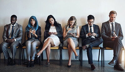 Buy stock photo Shot of a group of well-dressed businesspeople using their smartphones while waiting to be interviewed