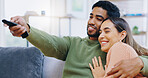 Couple, watching tv and remote on living room sofa with smile, hug or relax with click for choice, show or film. Man, woman and happy together for embrace, movie or streaming on lounge couch in home