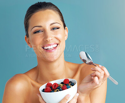Buy stock photo Studio shot of an attractive young woman eating a bowl of muesli and fruit against a blue background