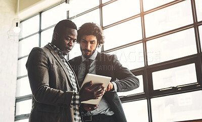 Buy stock photo Shot of two well-dressed businessmen brainstorming together over a tablet in their office