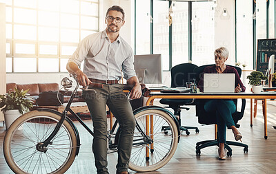 Buy stock photo Portrait of a mature businessman standing in a modern office with his bicycle