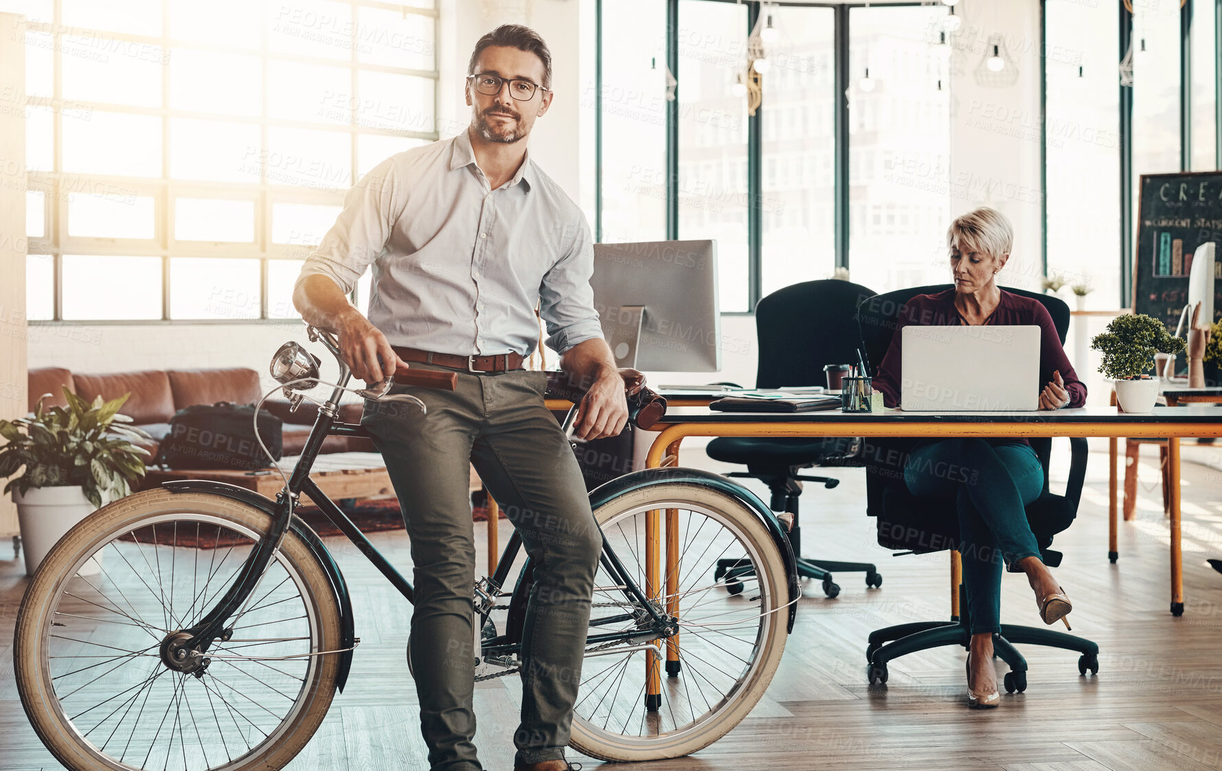 Buy stock photo Portrait of a mature businessman standing in a modern office with his bicycle