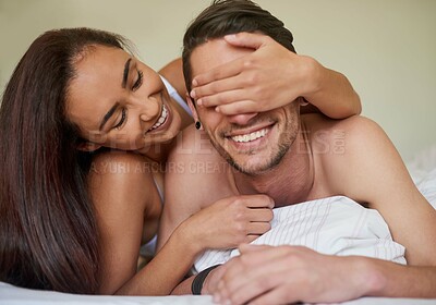 Buy stock photo Shot of a playful young woman covering her boyfriend's eyes while they lie in bed together