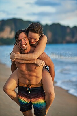 Buy stock photo Portrait of a happy young man giving his girlfriend a piggyback ride on the beach