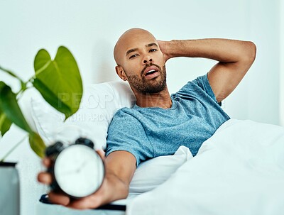 Buy stock photo Cropped shot of a man holding up his alarm clock while lying in bed