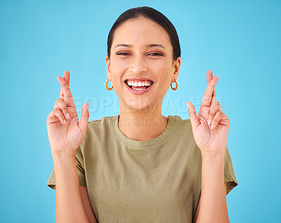 Buy stock photo Woman, cross fingers and studio portrait for smile, emoji or sign for hope by blue background. Girl, person and hands for good luck, wish or excited with icon, symbol or faith for results in contest