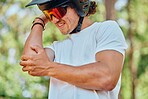 Sport, injury and man with arm pain, problem or issue while cycling in a forest on blurred background. Injured, elbow and male cyclist suffering inflammation, arthritis or joint ache during exercise