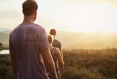 Buy stock photo Friends, people hiking and trekking in countryside with fitness at sunset, nature with travel together and freedom. Exercise, adventure with men and woman walk through meadow or field with back view