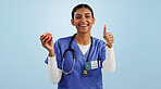 Happy woman, portrait and doctor with thumbs up for apple, health or diet against blue studio background. Female person, medical nurse or surgeon smile with like emoji or yes sign for organic fruit