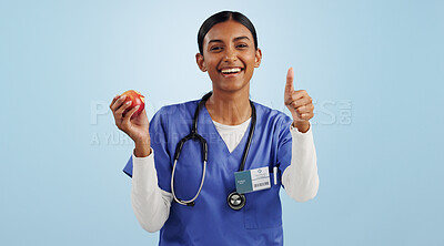 Happy woman, portrait and doctor with thumbs up for apple, health or diet against blue studio background. Female person, medical nurse or surgeon smile with like emoji or yes sign for organic fruit