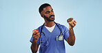 Doctor, man and studio for donut, apple and choice with thinking for healthcare by blue background. Medic, person or nutritionist with decision, cake and fruit with ideas for food, eating and diet