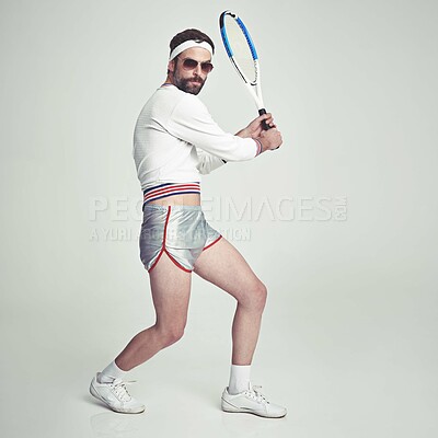 Buy stock photo A young man in the studio wearing ill-fitting retro tennis wear and shades while holding a racquet