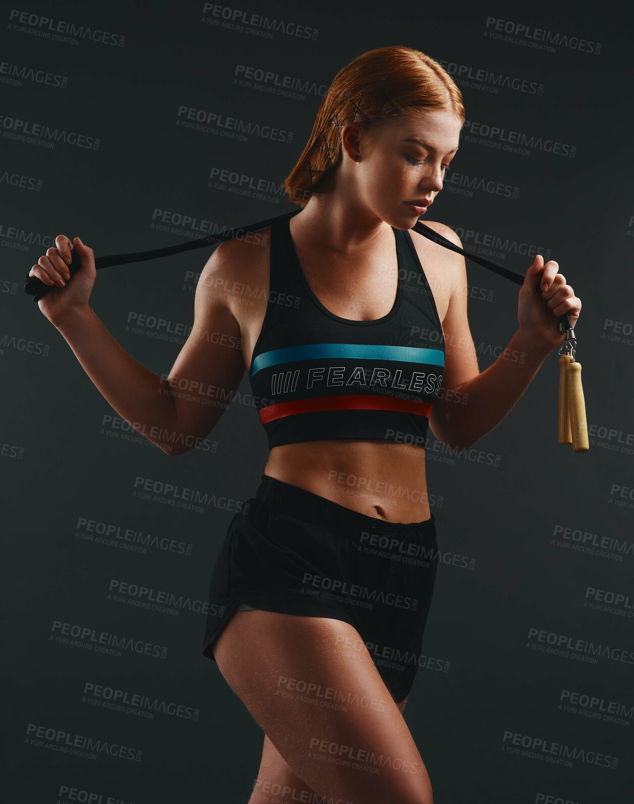 Buy stock photo Studio shot of a sporty young woman posing with a skipping rope against a black background