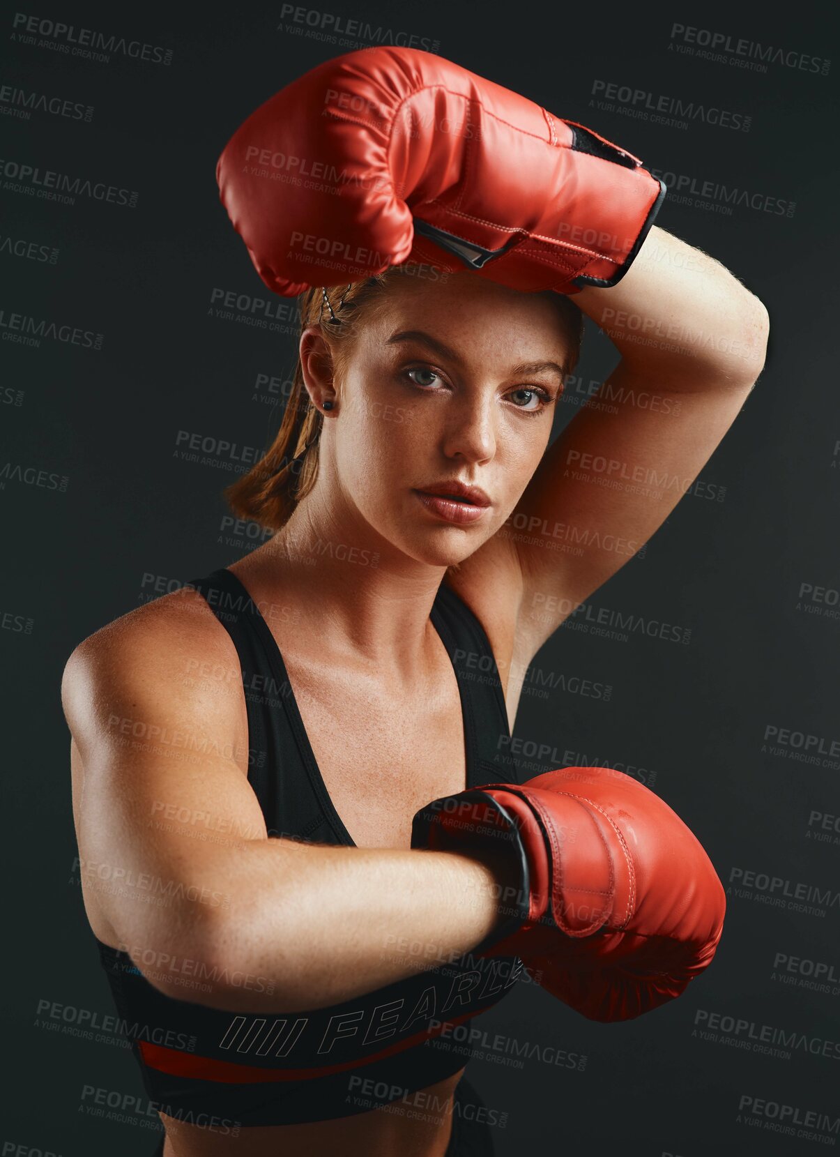 Buy stock photo Studio portrait of a sporty young woman wearing boxing gloves against a black background