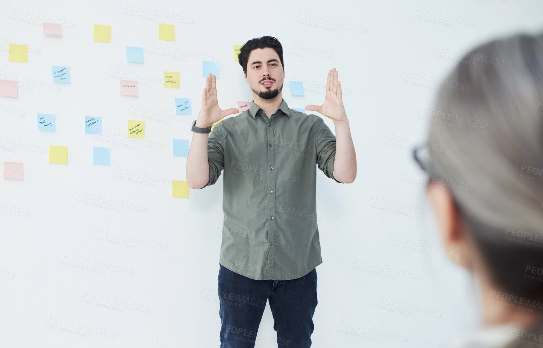 Buy stock photo Shot of a young businessman giving a presentation while standing against a wall with notes in an office