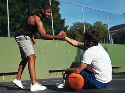 Buy stock photo Shot of two sporty young men shaking hands on a basketball court